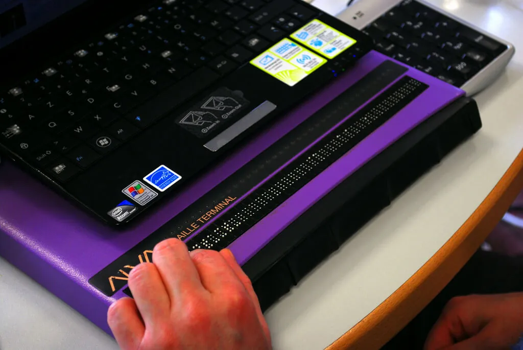 Person using a braille terminal linked to a screen reader with their laptop